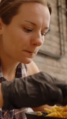 Dikey video. Siyah Eldivenli Kadın, Peynirli Isırıktan Zevk Alırken Rahatlatılmış Kafe Düzeninde Yemeğinin Tadını Çıkartıyor.