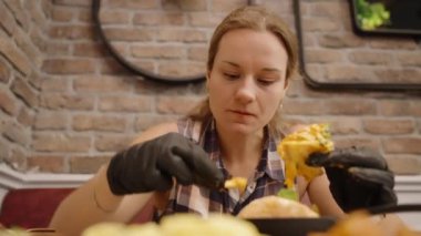 Siyah Eldivenli Kadın Fransız kızartması yiyor, Samimi bir kafede peynirli burgerden bir ısırık alıyor..