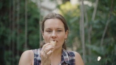Kadın, güneşli bir günde yemyeşil ile çevrili açık havada dondurma külahını seviyor..