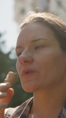 Dikey video. Kadın açık havada dondurma külahının tadını çıkarıyor, Güneşin ve Taze Çevrenin tadını çıkarıyor.