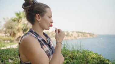 Kadın bir lolipop tutuyor, Düşünceli bir ifadeyle Manzaralı Su Manzarasına bakıyor..