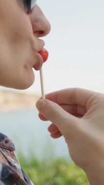 Dikey video. Lolipop Yiyen Kadın 'ın Yakın Çekimi Arkaplanda Güzel Bir Rıhtımla Zevk Almak.