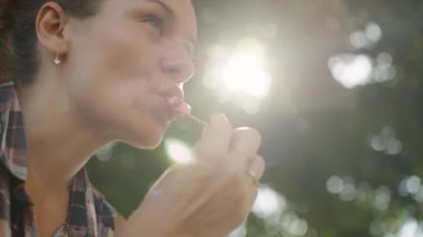 Kadın çizgili dondurmadan bir ısırık alır, Günışığının tadını çıkarır..