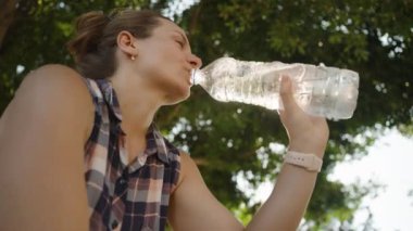 Kadın şişeden su içer, güneşli bir günde kendini tazeler..