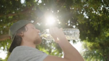 Adam Şişe 'den Suyu İçti, Gün Işığı Parkı' nda Ağaçların arasından Parlayan Güneş Işığı ile kendini tazeledi.