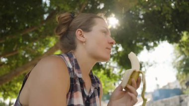 Kadın muzdan zevk alıyor, Parlak güneş ışığıyla gölgede dinleniyor Sıcak bir yaz gününde ağaçların arasından akıyor.