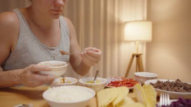 Kadın rahat bir evde taco hazırlıyor, taco kabuğuna domates sosu ekliyor..