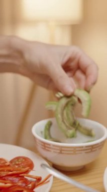 Dikey video. Kadın Taco Kabuğuna Avokado Dilimleri Ekliyor, Taze ve Lezzetli Taco Hazırlıyor.