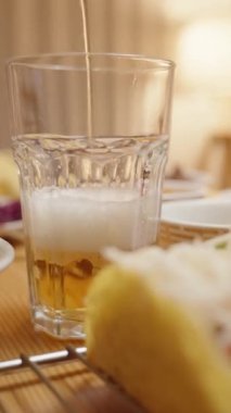 Dikey video. Bira, renkli sebzeler ve peynirle doldurulmuş takoların eşlik ettiği köpüklü bir kafa yaratan bir bardağa dökülüyor..