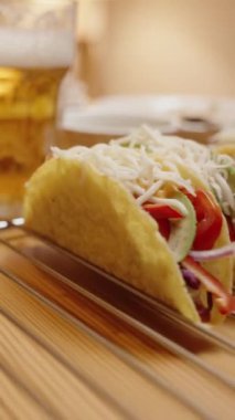 Dikey video. Köpüklü bir bardak bira Taze Taco ve Malzemeler 'in ortasında duruyor, Samimi bir akşam yemeği düzenliyor.