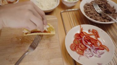 Taze sebzeler, peynirler ve lezzetli bir tabak için öğütülmüş et ile çevrili bir tako kabuğuna doğranmış tavuk ekler..