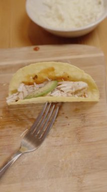 Dikey video. Bir El, Dilimlenmiş Sebze ve Yer Eti ile çevrili Tavuk Dilimlenmiş Taco Kabuğuna Taze Avokado Dilimleri Ediyor.