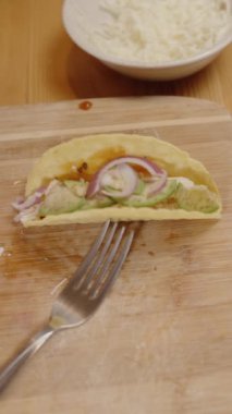 Dikey video. Bir Kişinin Eli Kırmızı Biber ve Soğanları Dilimlenmiş Taco Kabuğuna Koyuyor, Çeşitli Toplama ve Malzemeler Yakınlarda.