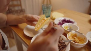 Bir Kişi Bir Taco Kabuğunu Yerden Etle Doldurur, Toplama için Çatal Kullanır, ve Masaya Çeşitli İçindekiler Kasesi.