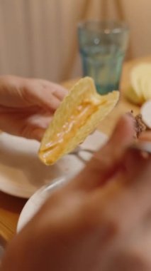 Dikey video. Bir Kişi Bir Taco Kabuğunu Yerden Etle Doldurur, Toplama için Çatal Kullanır, ve Masaya Çeşitli İçindekiler Kasesi.