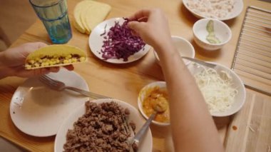 Eller bir taco kabuğunu mısır ve doğranmış kırmızı lahana ile doldurur, lezzetli ve renkli bir yemek hazırlar..