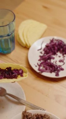 Dikey video. Bir El, mısır ve kırmızı lahana ile doldurulmuş Taco 'ya Taze Avokado Dilimleri Ekliyor, Lezzetli Taco Hazırlıyor.