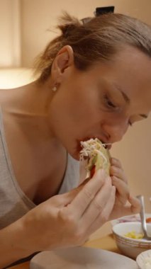 Dikey video. Bir Kadın Ev Yapımı Taco 'nun Lezzetli Isırığından Hoşlanıyor, Çeşitli Toplama ve İçindekiler Kâseleriyle çevrili..