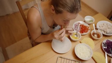 Taze sebze ve peynirle dolu, çeşitli malzemelerle dolu bir masada oturan bir kadın Taco 'nun tadına bakar..
