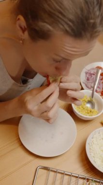 Dikey video. Taze sebze ve peynirle dolu, çeşitli malzemelerle dolu bir masada oturan bir kadın Taco 'nun tadına bakar..