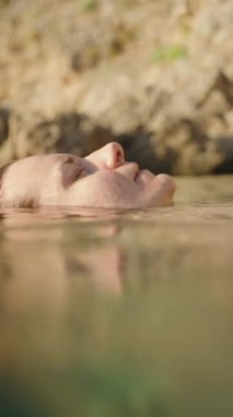 Dikey video. Yüzü Yüzeyin Altında Yüzen Bir Kadının Sualtı Görünümü, Saçları ve Çiçekli Bikini Üstü Güneş Işığı Suyu ile Güzel Bir Karşıtlık Oluyor. Yavaş çekim.