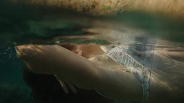 Suda Yüzen Bir Kadının Üst Gövdesinin Yakın Çekimi, Saçları ve Bikini Üstü Açıkça Görünür, Işık ve Su Dalgalanmaları Oyunuyla Vurgulanır. Yavaş çekim.
