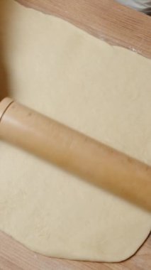 Dikey video. Dough 'u büyük bir dikdörtgen şeklinde tahta bir oklava ile düzleştirip, Eşitliğin Kalınlığını Sağlama.