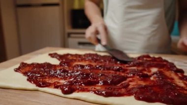 Hamur 'a vişne reçeli serpmek için Kara Spatula kullanmak, tüm yüzey kaplamalarını güvence altına almak.