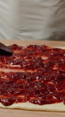 Dikey video. Siyah bir Spatula ile Cömertçe Vişne Reçeli Yaymak, Yuvarlanmaya ve Pişirmeye Hazırlanmak.