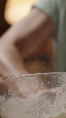 Dikey video. Un, bir kâsede hararetle karıştırılarak, un tozu bulutu oluşturur, yoğun hazırlık gösterir. Yavaş çekim.