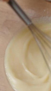 Dikey video. Cam kâse içindeki pürüzsüz kremalı hamur işi kişi pişirmeye hazırlanıyor, karıştırma tekniklerine odaklanıyor. Yavaş çekim.