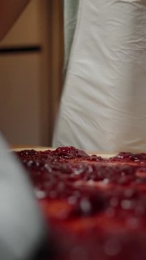 Dikey video. Black Spatula 'yla vişne reçelini Rolled Dough' a sürüyorum, Tatlı Doldurmaya hazırlanıyorum. Yavaş çekim.