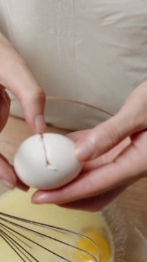 Dikey video. Yumurta sarısını cam kase, çırpma ve karışım karışımına ekleyen kişinin yakın çekimi, pişirme hazırlığı gösteriliyor. Yavaş çekim.
