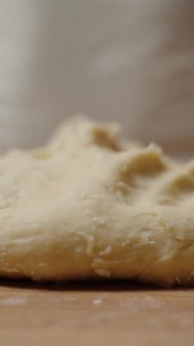 Dikey video. Tahta bir yüzeydeki elleri yassılaştıran Hamur, Hamuru pişirmek için şekillendirmeye hazırlanıyor, hatta dokuyu sağlamlaştırıyor. Yavaş çekim.