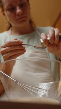 Dikey video. Bir kaşık ile fırın tozunu ölçmek, Fırın Tarifi için büyük bir cam kasede hamura eklemek..