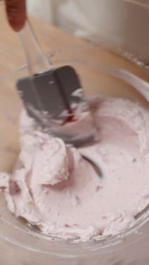 Dikey video. Vişne reçelini krema ile karıştırmak, Pembe vişne aromalı buzlanma yaratmak. Yavaş çekim.