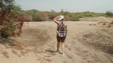 Kuru Yolda Yürüyen Bir Kadın, Kurumuş Sebzelerle çevrili Kumlu Yol Saçları ve Şapkası Onu Güneşten Koruyor.