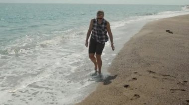 Kumsalda yürüyen bir kadın Dalgalar nazikçe ayaklarına dokunurken kumsalda geziniyor..