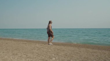 Bir kadın kumsalda yürüyor, okyanus manzarasının tadını çıkarıyor, uzak sularda görünen teknelerle..