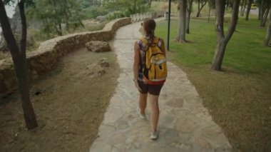 Deniz kıyısındaki taş bir yolda yürüyen bir kadın, elinde bir su şişesiyle huzurlu bir yürüyüşün tadını çıkarıyor..