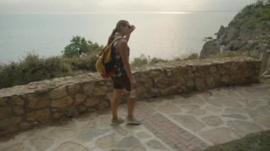 Deniz kenarında yürüyen bir kadın, taştan yolda yürürken yansıtan güneş ışığı....
