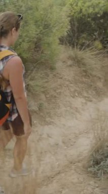 Dikey video. Bir Yürüyüşçü, Yoğun Çalılarla çevrili Rüzgarlı Toprak Yol 'da Gezinir. Olaysız Topraklarda Dikkatlice Yürür, Önündeki Yola Odaklanır.