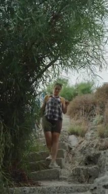 Dikey video. Yeşilliklerle çevrili Taş Merdivenlerden Dikkatle İnen Bir Kadın. Dar Yol 'da Dar Yol' da ilerlerken Nazikçe Dalları Uzağa itiyor.