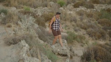 Kurutulmuş sebzelerle çevrili bir Rocky yamacında dikkatlice gezinen bir gezgin. Yoluna nazikçe devam eder, Köklerine konsantre olur..