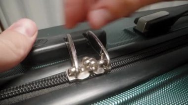 Bir El, valizin kombinasyon kilidinden fermuarı dikkatlice çıkarır ve güvenli bir yolculuktan sonra paketlenmiş içeriğe erişmeye hazırlanır..