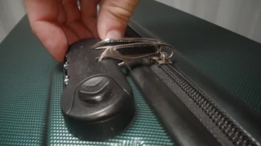 Bir El kilidin üzerindeki doğru kombinasyonu dikkatlice seçer, fermuarı açıp valizi açmaya hazırlanır.
