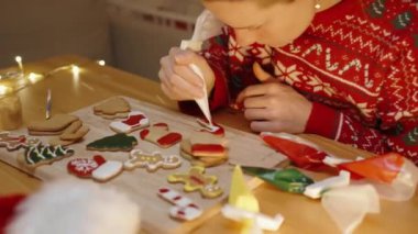 Kırmızı kazaklı bir kadın, Noel kurabiyesini süslemek için beyaz buzlu şekeri kullanırken konsantre oluyor. Sıcak evine şenlikli bir his getiriyor..