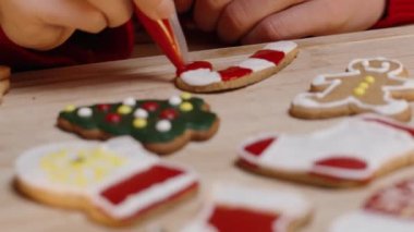 Bir Kadın Şeker Çubuğu Kurabiyesine Kırmızı Buzlu Şekerleme Ekliyor, Etrafı Şenlikli Kurabiyelerle çevrili.