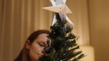 Kırmızı Süveterli Kadın Küçük Noel Ağacı Arkasında, Süs ve Işıkları Dikkatle Ayarlıyor.