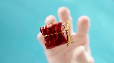 Bir El, Küçük Kırmızı Paketli Bir Hediye Sunar, Altın bir kurdeleyle bağlanmış, Noel Kutlamaları İçin Mükemmel.